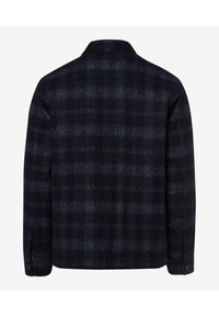 La veste à carreaux foncé présente un mélange de tons bleu marine et gris, avec des poignets à boutons et un col classique. Tissu doux avec une finition texturée.