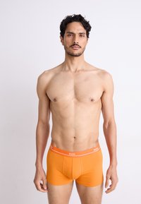 Orange bomulds boxer briefs med tætsiddende design, der har et hvidt "BOSS" logo bånd og en glat overflade. Ingen yderligere mønstre eller detaljer.