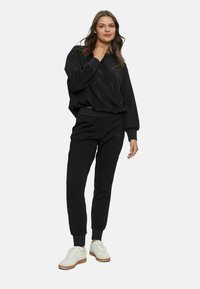 Set di felpa nera e pantaloni jogger realizzato in tessuto morbido. Vestibilità ampia, polsini a coste e dettagli sottili. Abbinato a sneakers bianche.