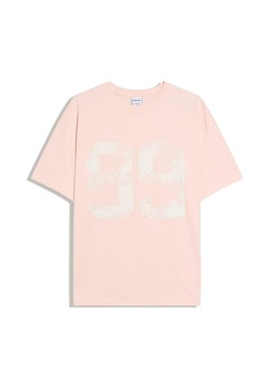 T-shirt à manches courtes rose clair avec un "90" blanc délavé et un texte en script imprimé sur le devant, col ras du cou et coupe décontractée.