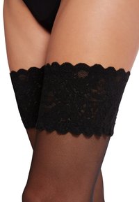 Sorte lårhøje strømper med blonder i toppen og en bølget kant. Gennemsigtigt sort materiale på benet, detaljeret blonderarbejde øverst.