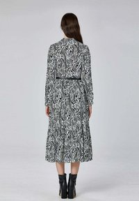 Robe à manches longues en imprimé zèbre noir et blanc avec une jupe à volants et une taille marquée, portée avec des bottes noires à talons épais.