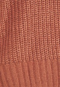 Gros plan d'un tissu tricoté marron avec une texture côtelée et des motifs de points verticaux.