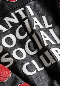 Czarna skórzana tkanina z dużymi białymi haftowanymi literami "ANTI SOCIAL SOCIAL CLUB" oraz czerwonymi naszywkami w kształcie róż.