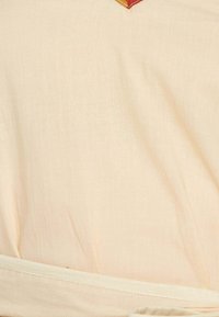 Haut en tissu couleur crème présentant une texture lisse, une ceinture à la taille et un accent triangulaire coloré près de l'encolure.