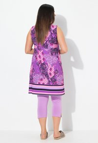 Barevná bezrukávová tunika s paisley vzorem v odstínech růžové a fialové, doplněná o světle fialové legíny do poloviny lýtek a ploché boty.