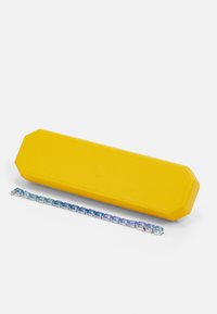 Caz galben octogonal alături de o brățară de argint cu pietre alternative albastre și turcoaz, evidențiind o textură netedă și reflectorizantă.