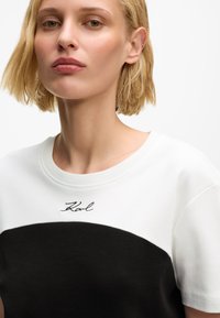 T-shirt z krótkim rękawem, z białą górną częścią i czarną dolną częścią, z haftowanym logo "Karl" na klatce piersiowej. Wykonany z miękkiej mieszanki bawełny.