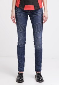Jeans skinny de denim azul con paneles verticales texturizados y parches en las rodillas, que cuentan con un diseño clásico de cinco bolsillos y un leve efecto de desgastado.