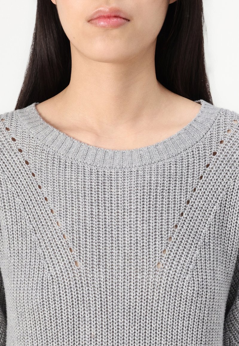 Szary sweter z dzianiny z okrągłym dekoltem, subtelnymi otwartymi wzorami na ramionach oraz teksturowanym, prążkowanym wykończeniem.