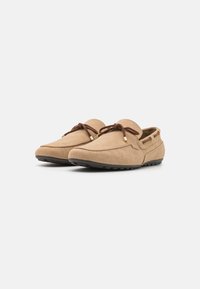 Tan suede loafers with a herringbone texture, rounded toe, lace-up design, and rubber sole featuring small grips. Gold-tone hardware accents.