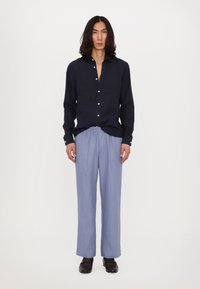 Marineblaues, lässiges Leinenhemd mit Knopfleiste; hellblaue, weit geschnittene Hose. Glatte Textur, minimalistisches Design, schwarze Slipper runden das Outfit ab.
