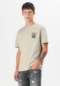 Light beige short-sleeve t-shirt made of soft cotton, featuring a black graphic print and small red accent on the sleeve.