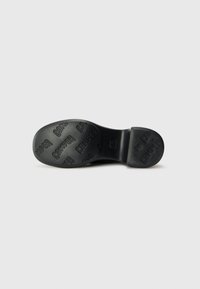 Black shoe sole featuring a smooth rubber material, with raised logos and text embossed on the surface, and a rounded heel design.