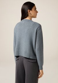 Lyseblå cropped sweater med rund halsudskæring og ribstrikkede manchetter, kombineret med mørkegrå, skræddersyede bukser. Glat tekstur og afslappet pasform.