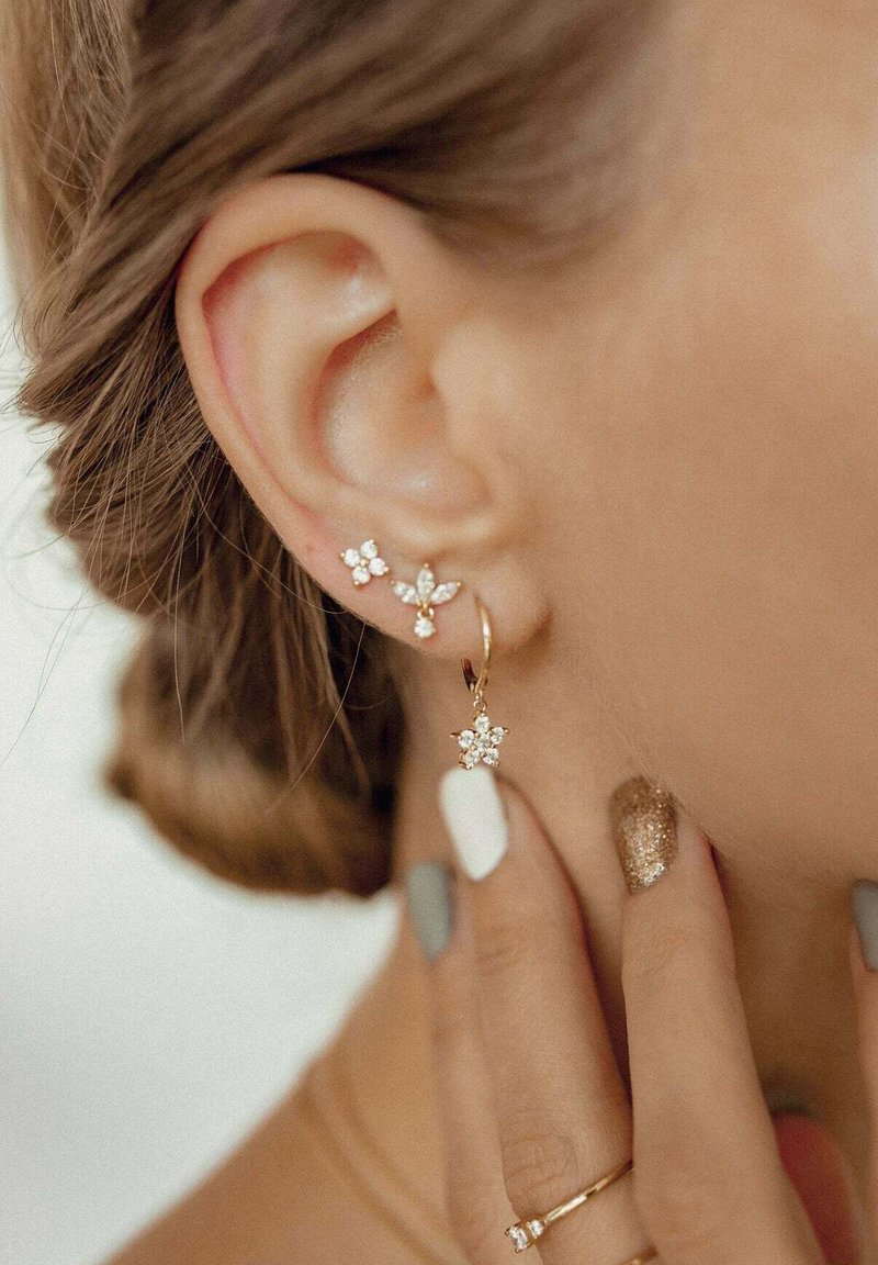 Gold hoop earring with a floral design, adorned with clear gemstones, alongside a smaller stud earring with a similar floral pattern.