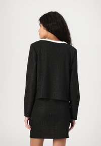 Černý metalický tweedový blazer s krojenou siluetou, kulatým výstřihem a hladkým bílým lemováním na zadní straně. Texturovaná tkanina.