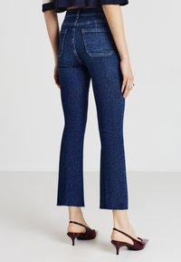 Jeans in denim scuro a zampa d'elefante con vita alta, dotati di due tasche posteriori e orlo grezzo, abbinati a mule con tacco color bordeaux.