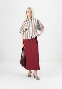 Camicia a maniche corte a righe in blu, arancione e bianco; gonna lunga bordeaux; decolletè grigi a punta; borsa scura.