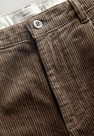 Pantaloni din corduroy maro cu o croială îngustă, textură ribbed verticală și un sistem de închidere cu un singur buton la talie.