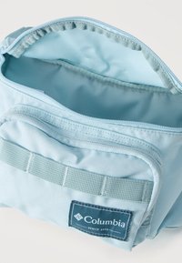 Φωτεινή γαλάζια υφασμάτινη θήκη Columbia με ανοιχτό φερμουάρ, μπροστινό λουράκι και εμφανές εσωτερικό επένδυμα.