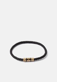 Bracelet en cuir tressé noir avec un fermoir magnétique cylindrique en or comportant le nom de la marque gravé sur fond blanc.