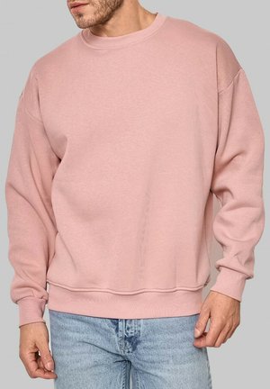 Sweatshirt rose clair à col rond avec des poignets et un ourlet côtelés, présentant une texture douce et une coupe ample, associé à un denim bleu clair.