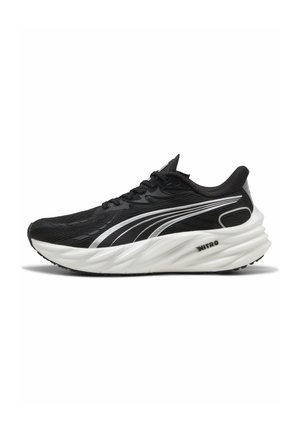Schwarze Sportschuhe mit einer strukturierten Oberseite, silbernen Akzenten und einer dicken, weißen, gepolsterten Sohle mit einem auffälligen Wellenmuster.
