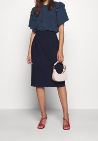 Marinblå prickig blus med korta volangärmar, högmidjad marinblå kjol, röda sandaler med remmar, och en liten ljusrosa handväska.