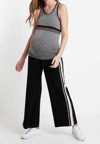 Graviditetstopp i grått med svarta detaljer, matchat med svarta vida byxor med vita sidsinglar och vita sneakers.