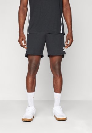 Zwarte sportshorts met een logo, gecombineerd met witte crew-sokken en witte sneakers. Het shirt is donker, met witte accenten aan de zijkanten.