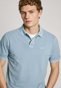 Light blue polo shirt made of soft fabric, featuring a classic collar, short sleeves, and subtle logo detailing on the front.