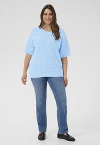Jersey de punto azul claro con patrón texturizado, mangas cortas y ajuste holgado, combinado con vaqueros azules de pierna recta y mocasines negros.