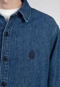 Camicia di jeans blu scuro, con colletto classico, chiusura a bottoni e ricamo logo sottile in filo scuro sul petto. Texture liscia.