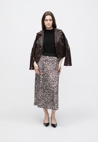 Giacca in pelle bordeaux con borchie e toppe, maglione a coste nero e gonna lunga con stampa leopardata. Look completato da tacchi neri.