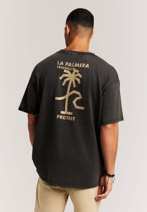 Zwart oversized T-shirt met een gouden afbeelding van een palmboom en de tekst "LA PALMERA BEACHCLUB PROTEST" op de achterkant. Gemaakt van katoen.