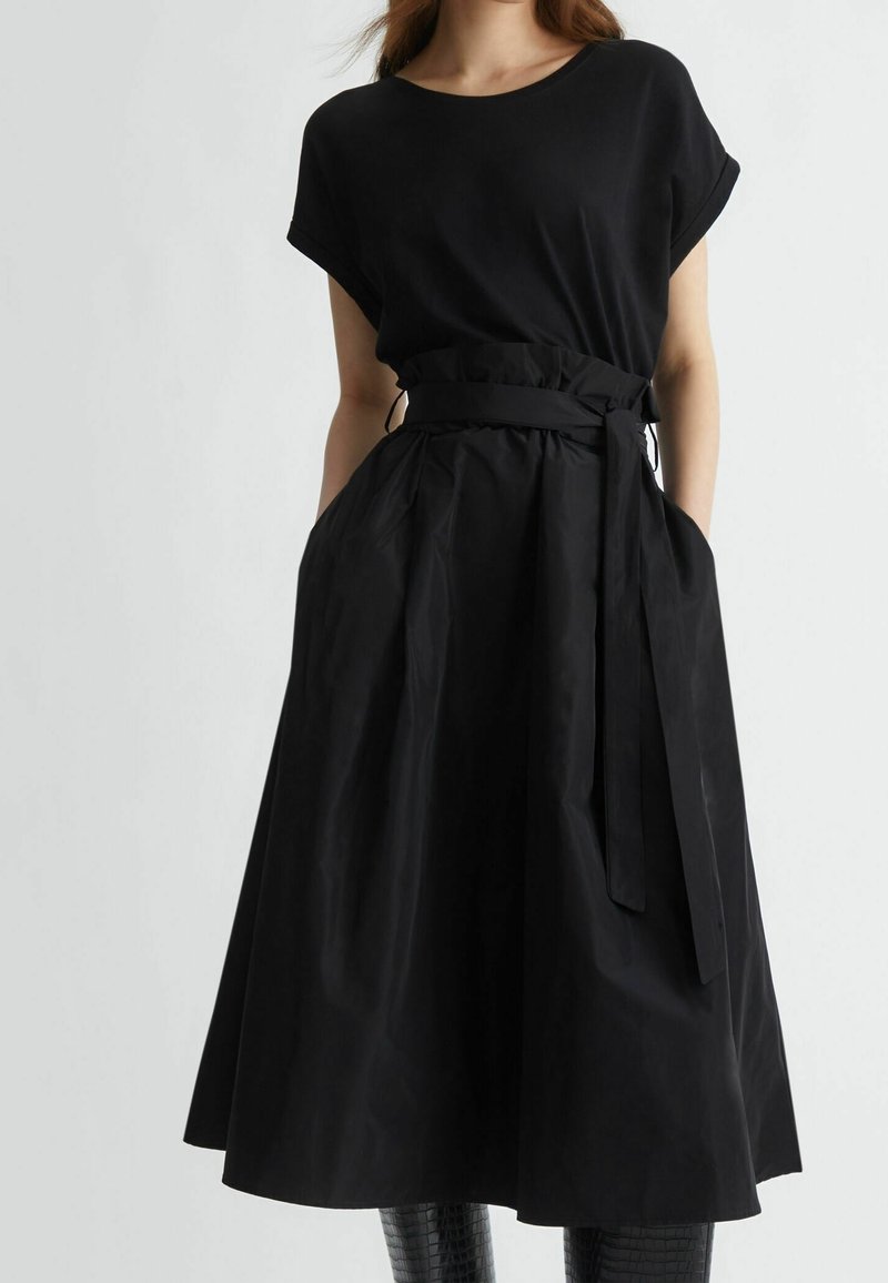Robe noire avec un haut ajusté et une jupe large évasée. Elle présente une taille ceinturée, des manches courtes et des poches latérales. Tissu à texture lisse.