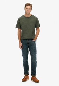 Olivengrøn bomuldstrøje med rund halsudskæring og korte ærmer, parret med blå denimjeans og brune snørebåndsstøvler.