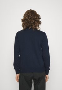Sudadera azul marino con cuello redondo, mangas largas y puños de canalé. Tejido suave con un corte relajado, mostrada desde la parte de atrás.