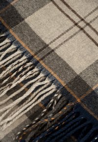 Wollen deken met een geruit patroon in grijs, beige en marineblauw, met franjes aan de randen en subtiele bruine accenten voor textuur.