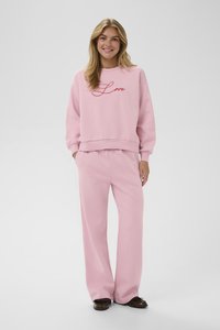 Svetlo roza pulover s vezenjem "Love" v rdeči barvi, v kombinaciji z ohlapnimi roza hlačami. Gladka tekstura, sproščen dizajn.