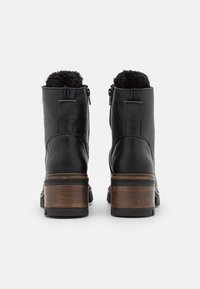 Zwarte leren enkelboots met een gestructureerde afwerking, nepbontvoering aan de bovenkant en bruine houten blokhakken. Zijritsen voor eenvoudig aantrekken.