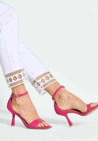 Roze hoge hakken sandalen gemaakt van glad materiaal hebben een smalle enkelriem en een open teen ontwerp. Gepaard met witte broeken met patroonranden.