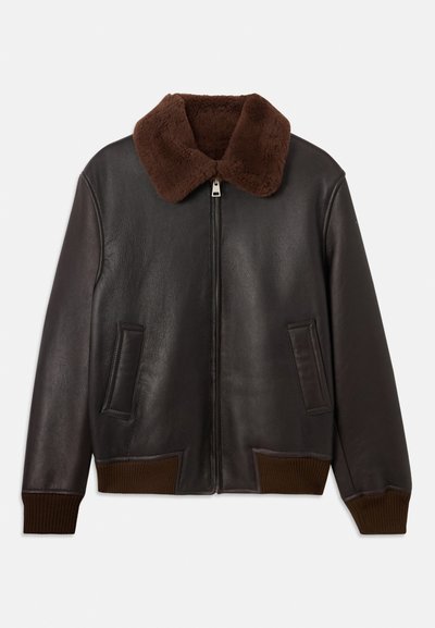 Brun læder bomberjakke med en krave af kunstpels. Har ribbede manchetter og nederkant, to forlommer og lynlås lukning. Glat tekstur.