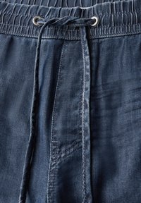 Modré džínové tepláky s elastickým pasem a šňůrkou, s hladkou texturou a detailním prošíváním podél švů.