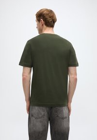 Λαδί κοντομάνικη μπλούζα με στρογγυλή λαιμόκοψη, κατασκευασμένη από απαλό βαμβάκι, με άνετη εφαρμογή και ελάχιστες ραφές.