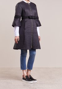 Vadderad knälång rock i mörkgrått, med dragkedja framtill och utsvängda ärmar. Kombinerad med korta blå jeans och svarta slip-on skor.