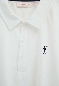 Biała koszulka polo z trzema guzikami, małym, granatowym haftowanym logo golfisty na piersi oraz metką "POLO CLUB" wewnątrz kołnierzyka.