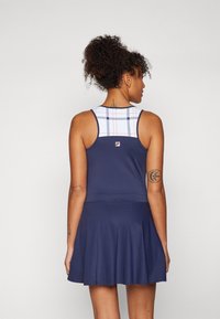 Temno modra teniška obleka ima oprijet zgornji del s karirastim vzorcem, razširjen krilo in detajl logotipa na hrbtni strani. Narejena je iz mehkega in raztegljivega materiala.