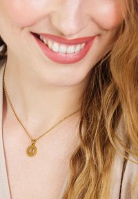 Gouden halsketting met een ronde hanger met een gegraveerd ontwerp. De ketting is delicaat en fijn geschakeld. Draag op blote huid.